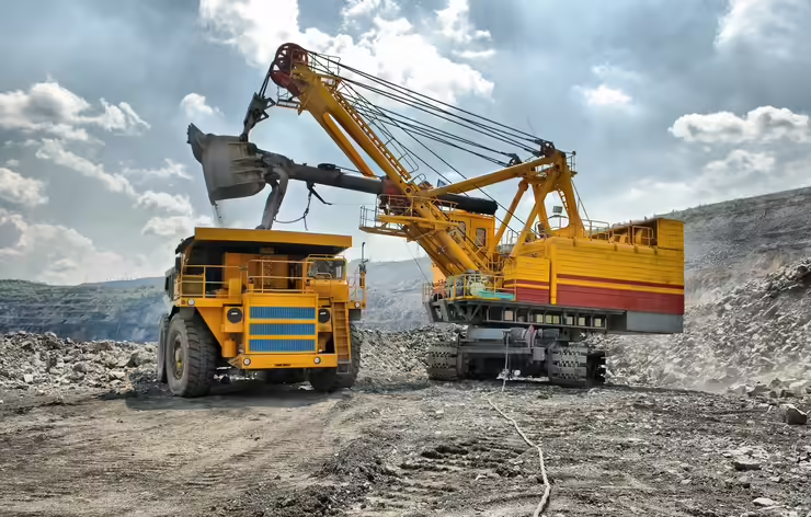 Massive yellow dragline excavator loading mining dump truck at open-pit mining operation
